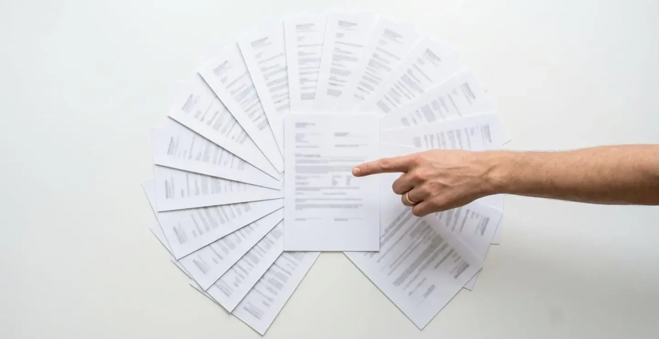 Vue aérienne d'une table avec différents documents officiels disposés en éventail, main pointant vers un document central